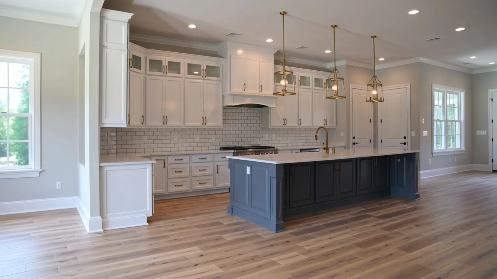 Remodeled kitchen with white shaker cabinets, a navy island and brass pendant lights