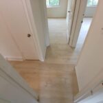 Hallway renovation featuring light wood floors and smooth white walls.